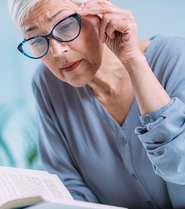 Senior woman adjusting glasses and trying to read a book