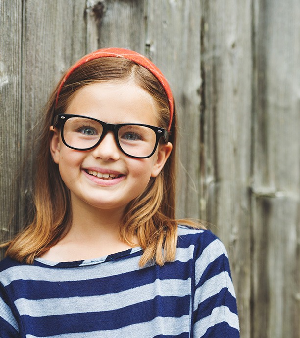 Little girl with glasses leaning against fence