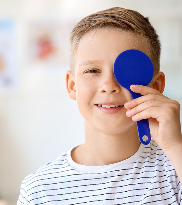 Little boy in striped shirt covering one eye for eye exam