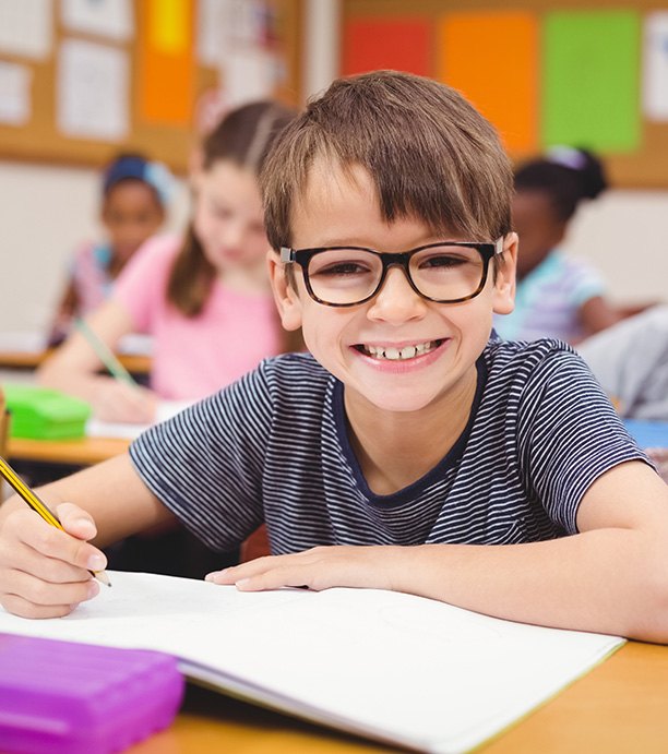 Little boy with glasses writing in notebook at school