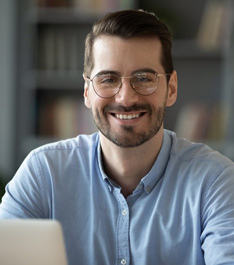Bearded man with glasses sitting at computer and smiling