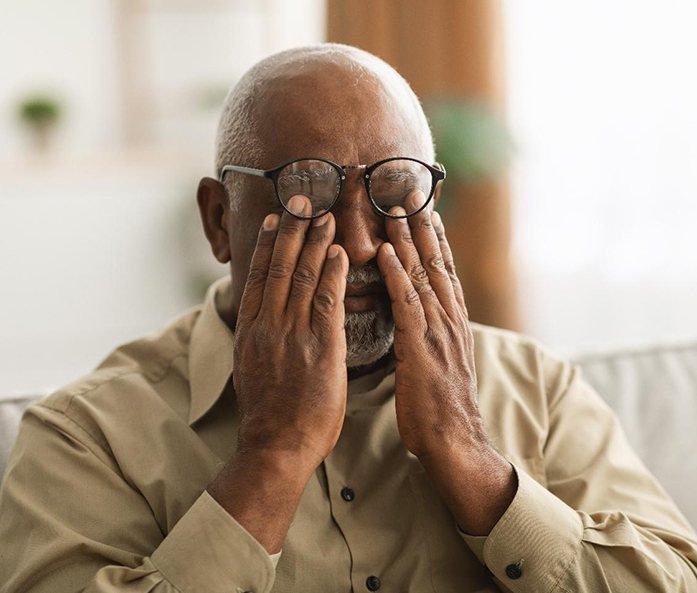 Man with glasses sitting on couch and rubbing his eyes