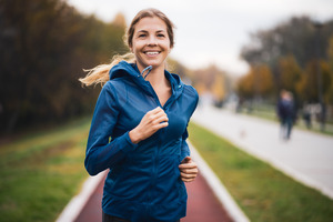 Woman in blue hoodie jogging down a dirt path